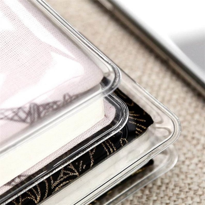 May include: Close-up of a clear plastic cover for a book. The cover is made of a thick, durable plastic and has a smooth, glossy finish. The cover is designed to protect the book from dust, dirt, and water damage.