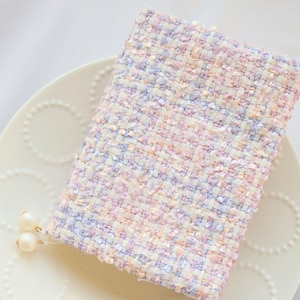 May include: A white, pink, and purple tweed fabric swatch on a white plate with pearl-like embellishments.