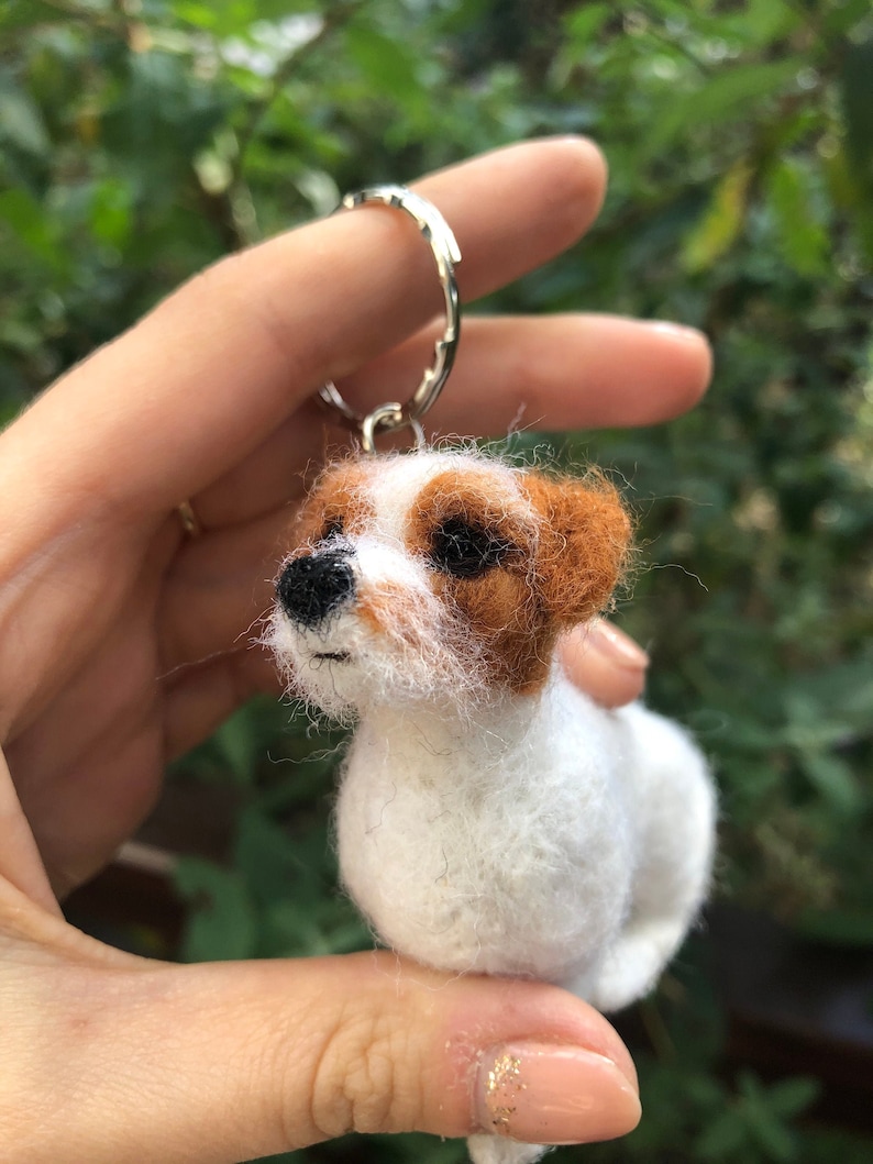 May include: A white and brown felt dog keychain with black eyes and a black nose.