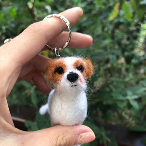 May include: A white and brown felt dog keychain with a black nose and brown eyes.