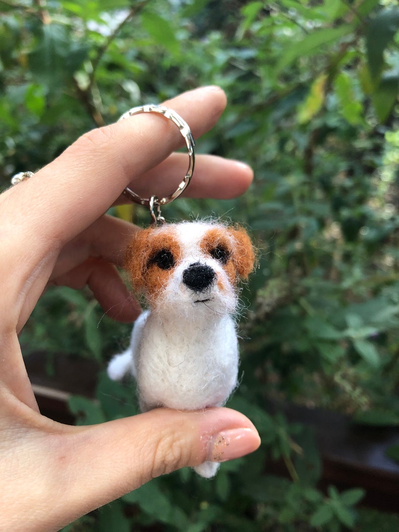 May include: A white and brown felt dog keychain with a black nose and brown eyes.