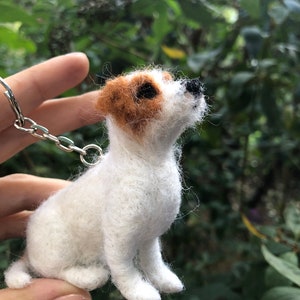 May include: A white and brown felt dog keychain with black eyes. The dog is sitting up and looking to the right. The keychain is attached to a silver chain.