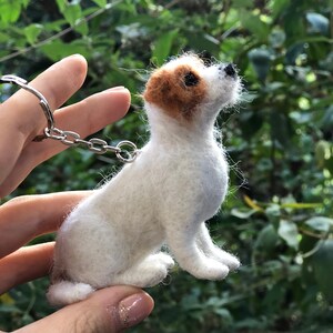 May include: A white and brown needle felted Jack Russell Terrier dog keychain. The dog is sitting up and looking to the right. The keychain is attached to a silver chain.