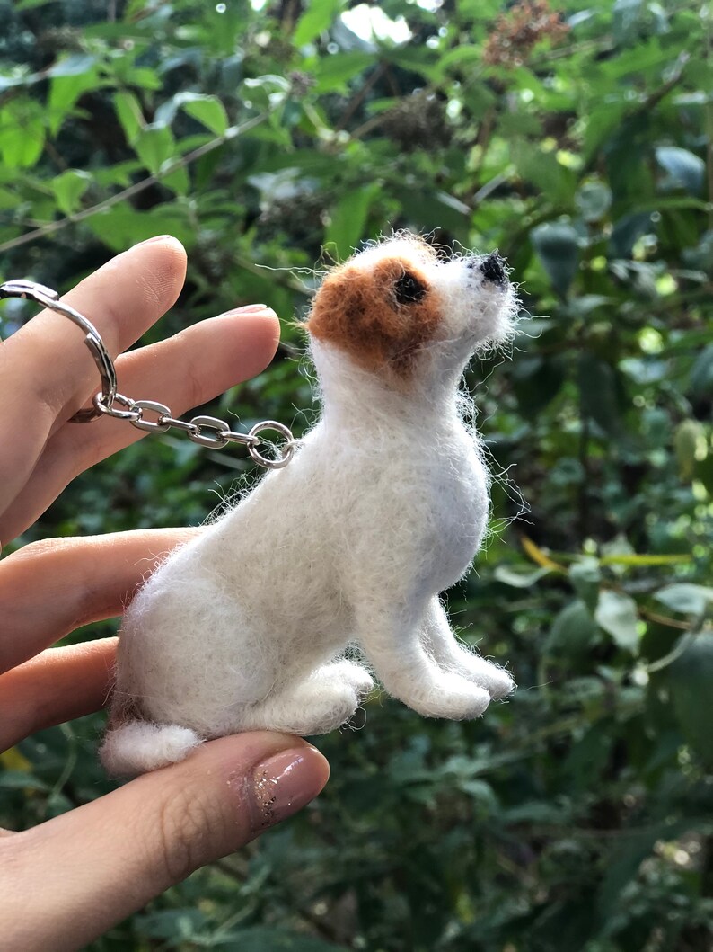 May include: A white and brown needle felted Jack Russell Terrier dog keychain. The dog is sitting up and looking to the right. The keychain is attached to a silver chain.