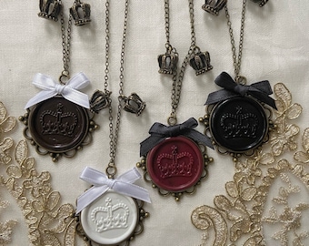 May include: Four necklaces with bronze chains and crown charms. Each necklace has a wax seal pendant with a crown design. The wax seals are in brown, red, white, and black.