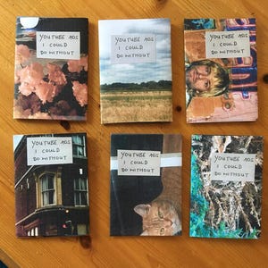 Puede incluir: Seis folletos rectangulares con portadas fotogr&aacute;ficas variadas, cada uno con una etiqueta blanca con el texto escrito a mano "YOUTUBE ADS I COULD DO WITHOUT". Las portadas muestran im&aacute;genes de flores rosas, un campo, una persona, un edificio, un gato y follaje.