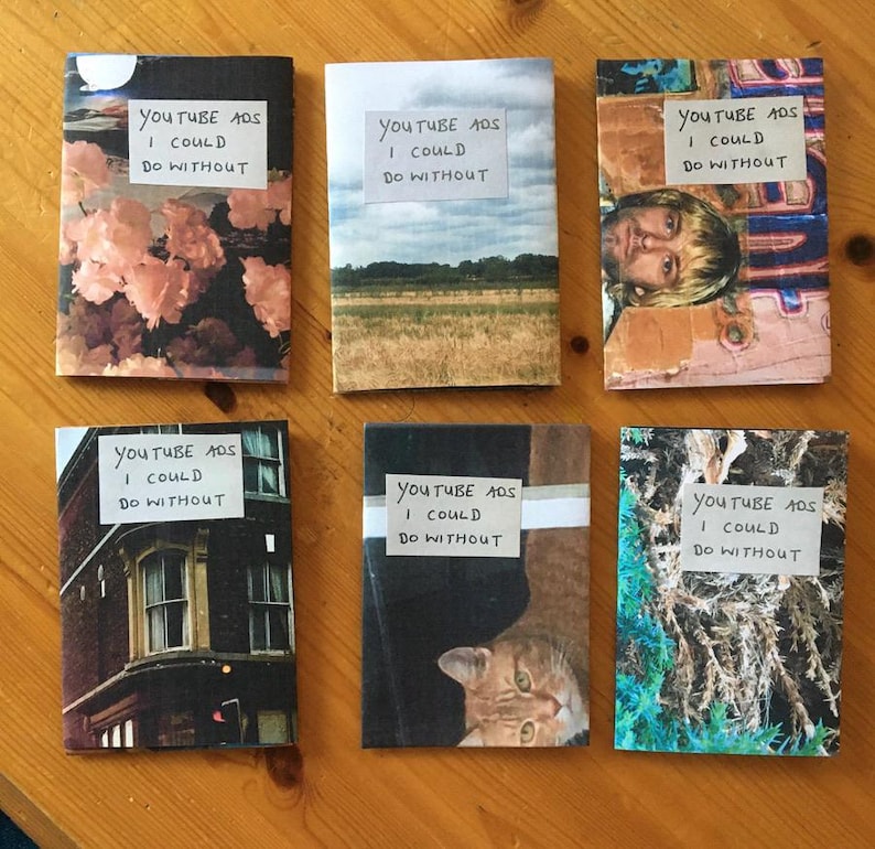 Puede incluir: Seis folletos rectangulares con portadas fotogr&aacute;ficas variadas, cada uno con una etiqueta blanca con el texto escrito a mano "YOUTUBE ADS I COULD DO WITHOUT". Las portadas muestran im&aacute;genes de flores rosas, un campo, una persona, un edificio, un gato y follaje.