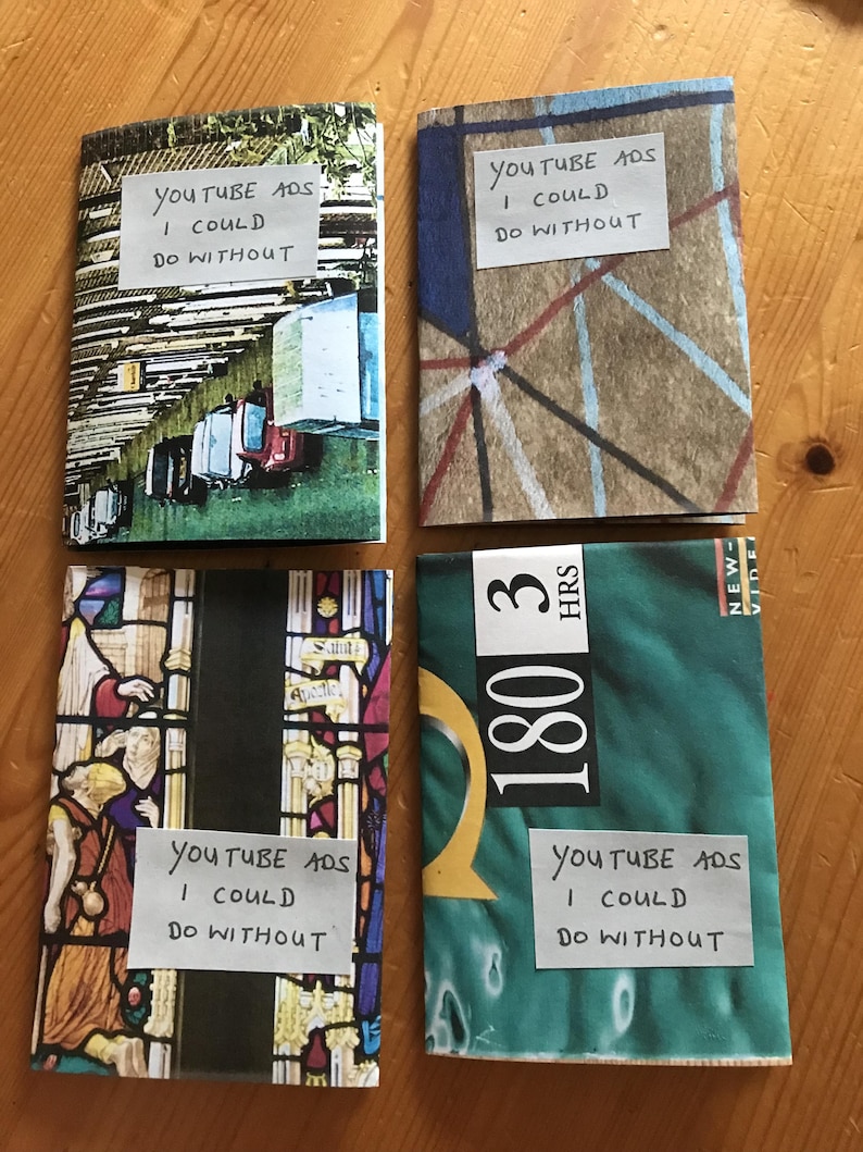 Puede incluir: Cuatro folletos rectangulares con dise&ntilde;os de portada variados. Cada folleto presenta una etiqueta de papel blanco con el texto escrito a mano "YOUTUBE ADS I COULD DO WITHOUT". Las portadas muestran una escena callejera, l&iacute;neas geom&eacute;tricas abstractas, vidrieras y un gr&aacute;fico verde con el texto "180 3 HRS".