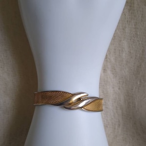 May include: A gold and silver toned bracelet with a woven design. The bracelet is on a white mannequin arm.