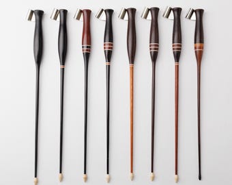 May include: Eight oblique calligraphy pen holders arranged in a row. Each holder features a turned wooden handle in various shades of brown and black, some with inlaid light-colored rings, and a silver-toned metal flange at the top for nibs.