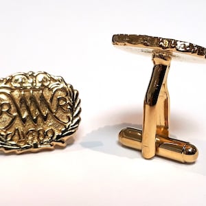 May include: Gold cufflinks with a circular design featuring the initials "RWR" and the year "1969" surrounded by a laurel wreath.