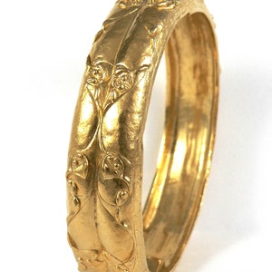 May include: A gold bangle bracelet with a floral design. The bracelet is made of solid gold and has a smooth, polished finish.