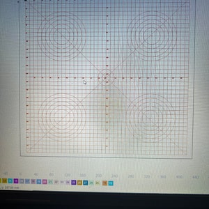 May include: A computer screen displaying a red grid pattern with concentric circles and intersecting lines. The design includes text and numerical values, likely for technical or design purposes. The screen is part of a larger setup.