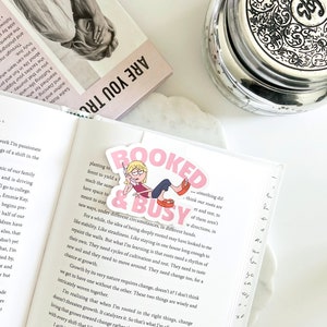 May include: A pink and white bookmark with a cartoon illustration of a woman on the phone. The bookmark has the text "BOOKED & BUSY" in large pink letters.