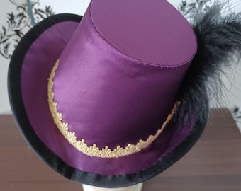 Può includere: Un cappello a cilindro viola con una piuma nera e un bordo dorato. Il cappello è su un supporto nero.