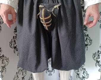 Op de afbeelding: Een paar zwarte wollen broek met een decoratieve zak aan de voorkant. De zak is gemaakt van bruin stof en heeft een gouden rand. De broek is getailleerd en heeft een trekkoord sluiting.