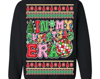 May include: Black sweatshirt with a festive design. The front features the text "IN MY CHRISTMAS ERA" in colorful, bubble-style letters, along with a disco ball and Christmas tree graphics. The top and bottom of the sweatshirt have a repeating pattern of Christmas trees.