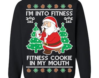 May include: Black sweatshirt with a graphic of Santa Claus holding a cookie and a glass of milk. The text reads "I'M INTO FITNESS" and "FITNESS COOKIE IN MY MOUTH". The design includes green Christmas trees, cookies, and weightlifting icons.