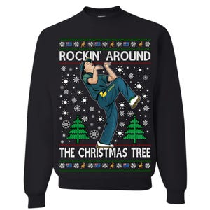 May include: Black sweatshirt with a festive design. The graphic features a person in green and yellow clothing, with the text "ROCKIN' AROUND THE CHRISTMAS TREE". The design includes snowflakes, Christmas trees, and Australian flag elements.
