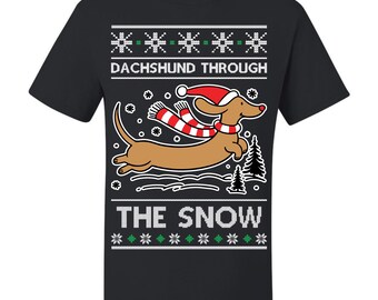 May include: Black t-shirt featuring a brown dachshund wearing a Santa hat and scarf, jumping through the snow. The text "DACHSHUND THROUGH THE SNOW" is printed above and below the dog in a festive font, with snowflake and evergreen tree graphics.