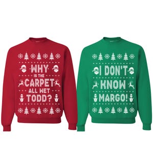 May include: Two Christmas sweaters with a white snowflake pattern. One sweater is red with the text "Why is the carpet all wet Todd?" and the other is green with the text "I don't know Margo!"