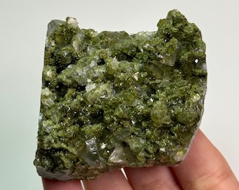 May include: A cluster of green and clear crystals, with a rough, natural texture. The crystals are arranged in a random pattern, creating a unique and interesting display.
