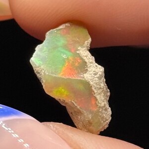 Könnte beinhalten: Ein roher, natürlicher Opal mit einem grün-orange-gelben, irisierenden Schimmer. Der Opal ist ein roher, unpolierter Stein mit einer rauen, unregelmäßigen Form.