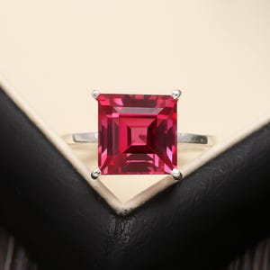 May include: A silver ring with a large, square, red gemstone.