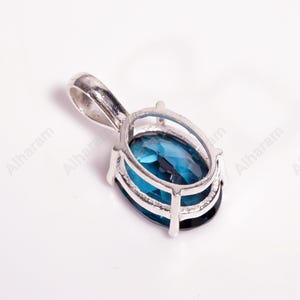May include: A silver pendant with a blue gemstone set in a silver frame. The pendant has a bail for attaching to a chain.