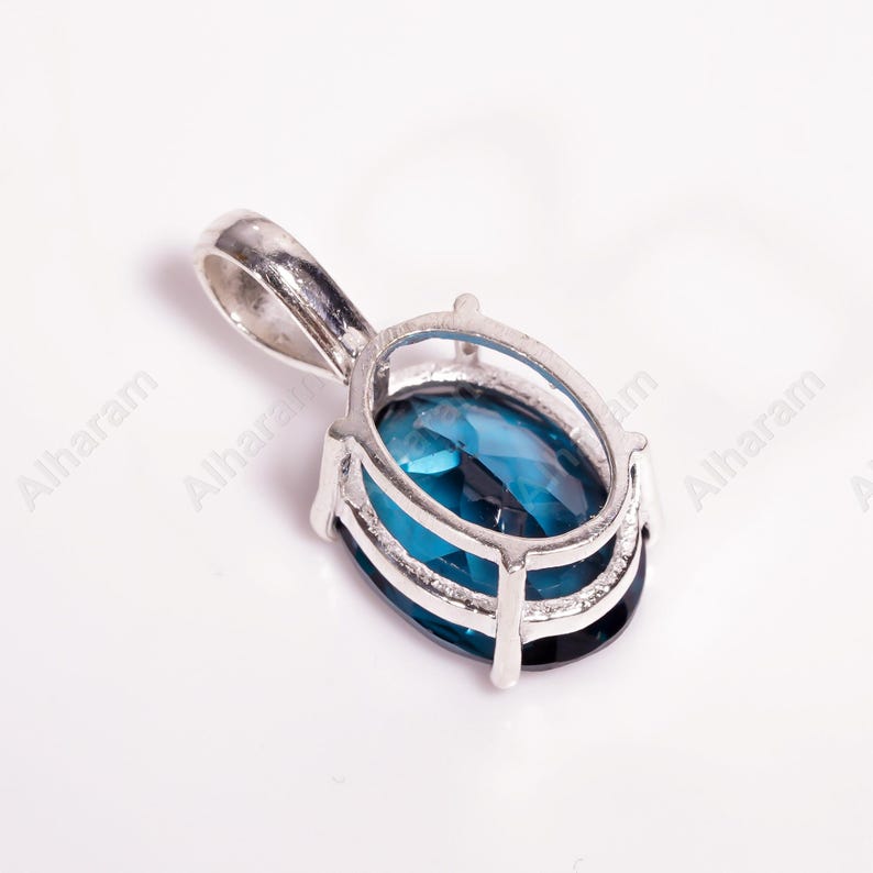 May include: A silver pendant with a blue gemstone set in a silver frame. The pendant has a bail for attaching to a chain.