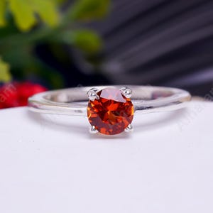 May include: A silver ring with a round, orange gemstone.