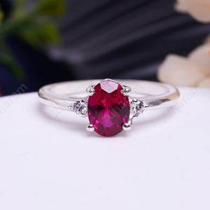 May include: A silver ring featuring a large oval ruby gemstone and two smaller diamond accents.