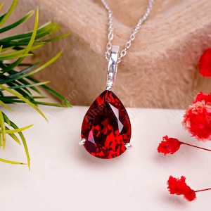 May include: A silver chain necklace with a teardrop-shaped pendant featuring a large, deep red gemstone.