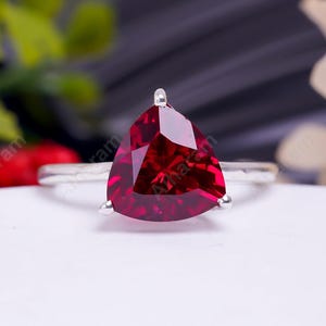 May include: A silver ring featuring a large, triangular, red gemstone.
