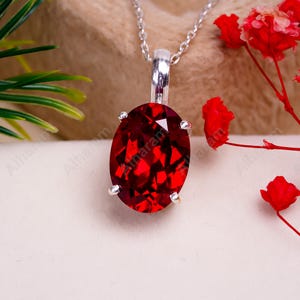 May include: A silver chain necklace with a pendant featuring a large, oval-shaped, red gemstone.