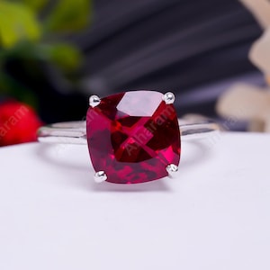 Op de afbeelding: Een zilveren ring met een grote, vierkante, rode edelsteen.