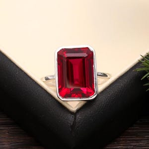 May include: A silver ring with a large, red, emerald-cut gemstone.