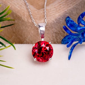 May include: A silver chain necklace with a round, red gemstone pendant.