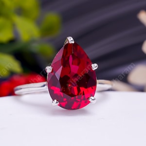 May include: A silver ring with a large pear-shaped red gemstone.