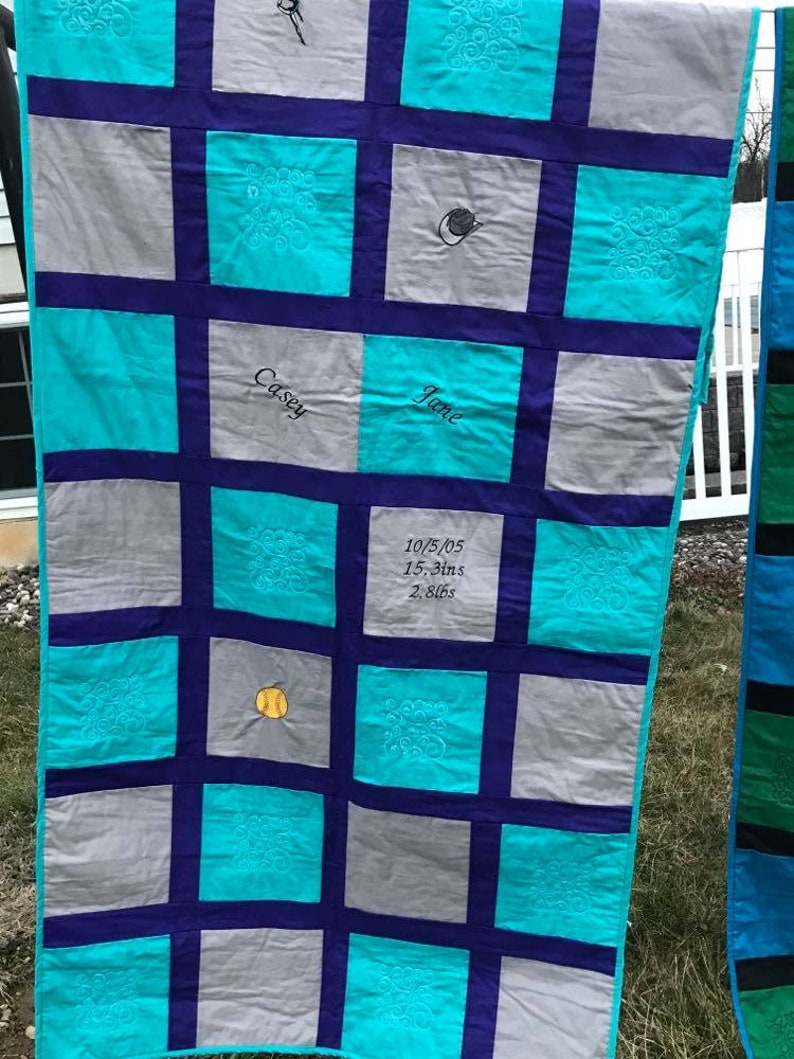 May include: A turquoise and gray quilt with a baseball, a pumpkin, and the names Casey and Jane embroidered on it. The quilt also includes the date 10/5/05, 15.3ins, and 2.8lbs.