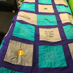 May include: A teal, purple, and gray patchwork quilt with embroidered designs. The quilt has a baseball, swirls, and the text "Casey", "Jane", and "10/5/05 15.3ins 2.8lbs".