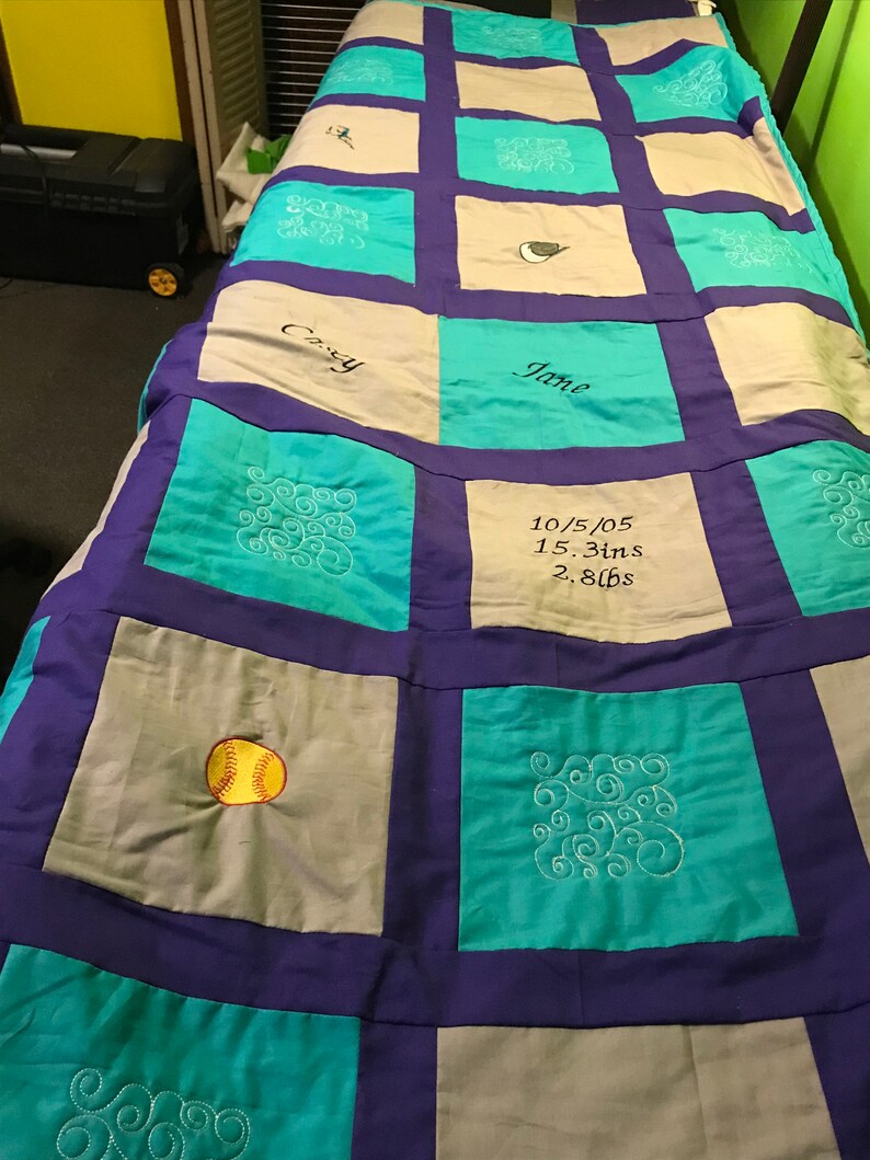 May include: A teal, purple, and gray patchwork quilt with embroidered designs. The quilt has a baseball, swirls, and the text "Casey", "Jane", and "10/5/05 15.3ins 2.8lbs".
