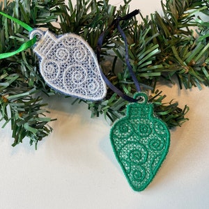 May include: Two embroidered Christmas ornaments in the shape of light bulbs. One is white with blue swirls and the other is green with white swirls.