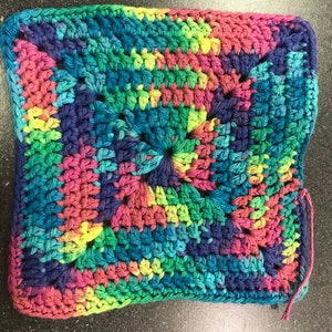 May include: A colorful crocheted square dishcloth with a multi-colored yarn in shades of pink, blue, green, and yellow.