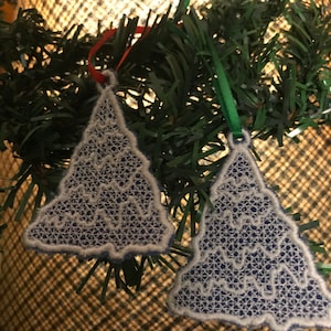 May include: Two white and blue lace Christmas tree ornaments with a green garland and a light brown background.