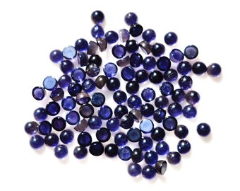 May include: A large group of small, round, dark blue gemstones. The gemstones are scattered on a white background.