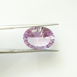 May include: A light purple oval-shaped gemstone held by tweezers. The gemstone is faceted and has a clear, glassy appearance.