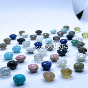 May include: Assortment of colorful gemstone cabochons in various shapes and sizes. The cabochons are polished and have a smooth, rounded surface. They are arranged in a random pattern on a white background. The text "gembasketin" is visible in the center of the image.