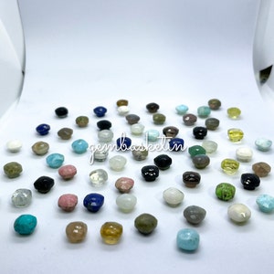 May include: Assortment of colorful gemstone cabochons in various shapes and sizes. The cabochons are displayed on a white surface.