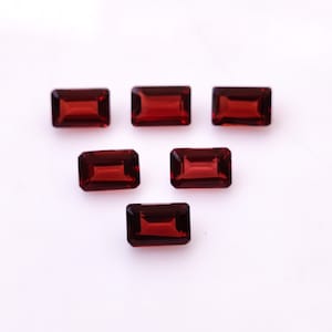 May include: Six red rectangular gemstones with a faceted cut. The gemstones are arranged in a triangular pattern on a white background.